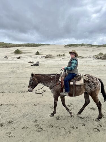 Equestrian travel expert Nancy D. Brown riding Ace, an Appaloosa horse with a spotted coat. She is walking her horse on Baker Beach in Florence, Oregon. 