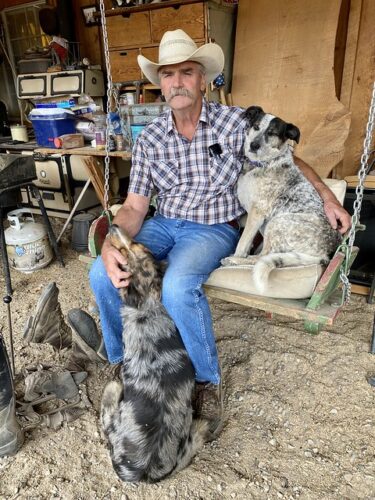 Cowboy Rodney Carriker on a porch swing at Canyon Trails Ranch surrounded by two ranch dogs in Cortez, Colorado.
